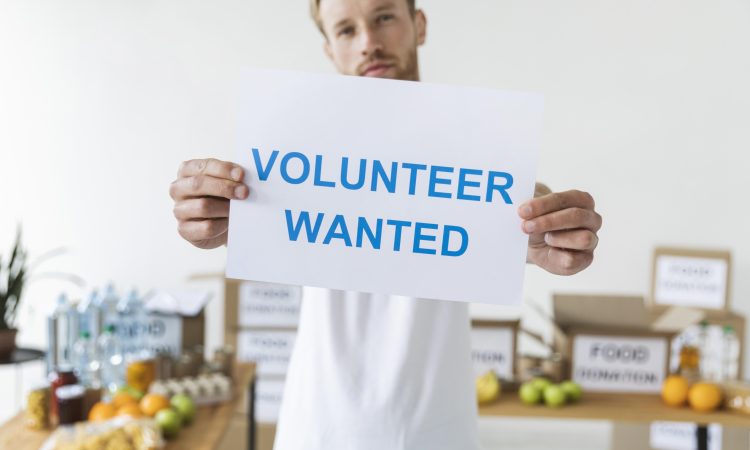 na slici je čovjek koji drži natpis ,,potrebni volonteri"