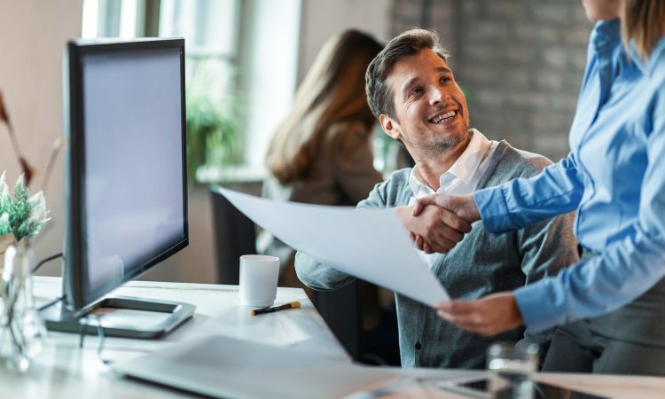 Happy businessman shaking hands with female colleague and congratulating her on excellent job she did.
