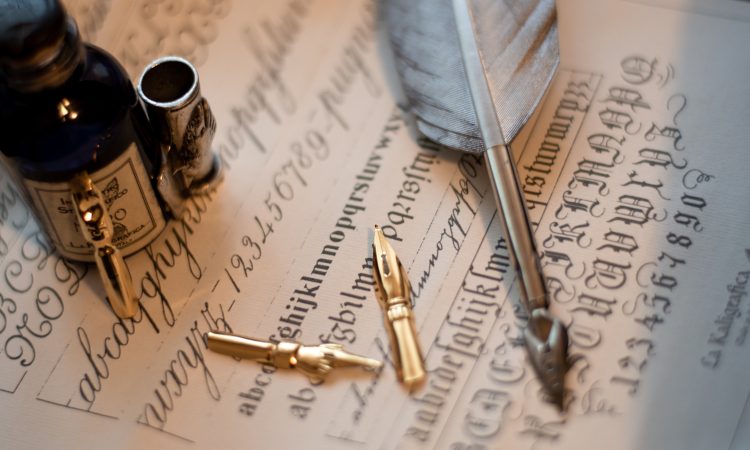 A macro shot of a quill set and an ink bottle on a piece of paper with calligraphy on it