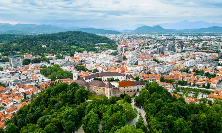 Aerial drone view of Ljubljana, Slovenia. Historical city centre with Ljubljana Castle, lush greenery and multiple residential buildings, hills on the background