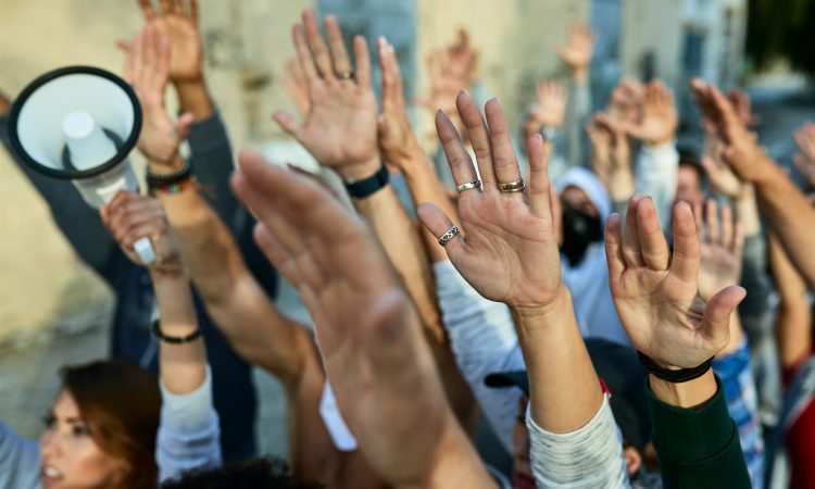 Close-up of crowd of protesters with arms raised demonstrating on the streets.