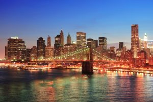 New York City Manhattan downtown skyline aerial view at dusk with skyscrapers lit over East River with reflections.