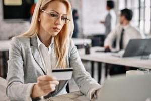 Serious businesswoman credit card and laptop to shop online while sitting at her office desk.