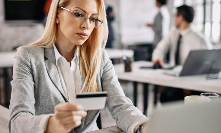 Serious businesswoman credit card and laptop to shop online while sitting at her office desk.