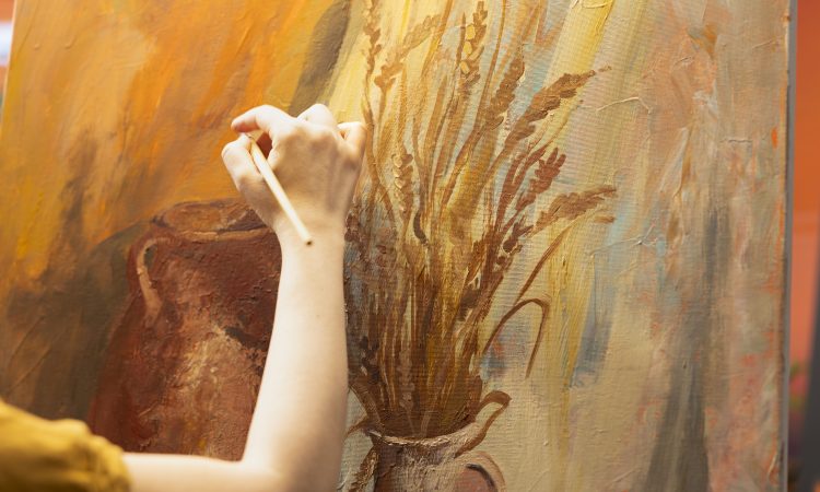 Artisan inspired by natural rural elements to paint a masterpiece on canvas, using modern paintbrushes in art studio. Working with motivation and creativity for fine art creative process. Close up.