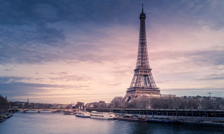 A beautiful wide shot of Eiffel Tower in Paris surrounded by water with ships under the colorful sky