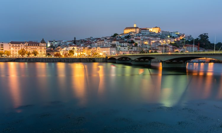 A bridge on the sea surrounded by Coimbra with the lights reflecting on the water in Portugal