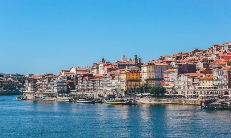 A wide shot of boats on the body of water near houses and buildings in Porto, Portugal
